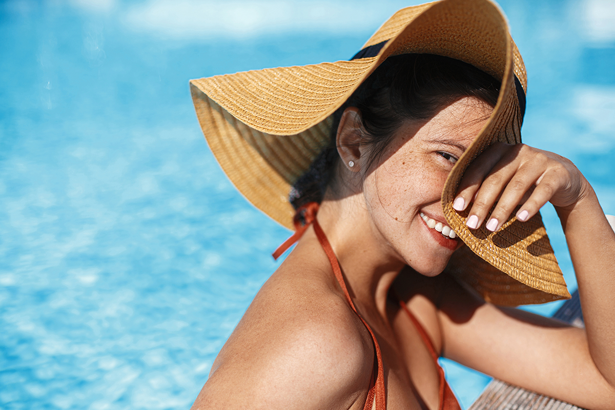 Beautiful happy carefree woman in hat relaxing in pool, enjoying summer vacation