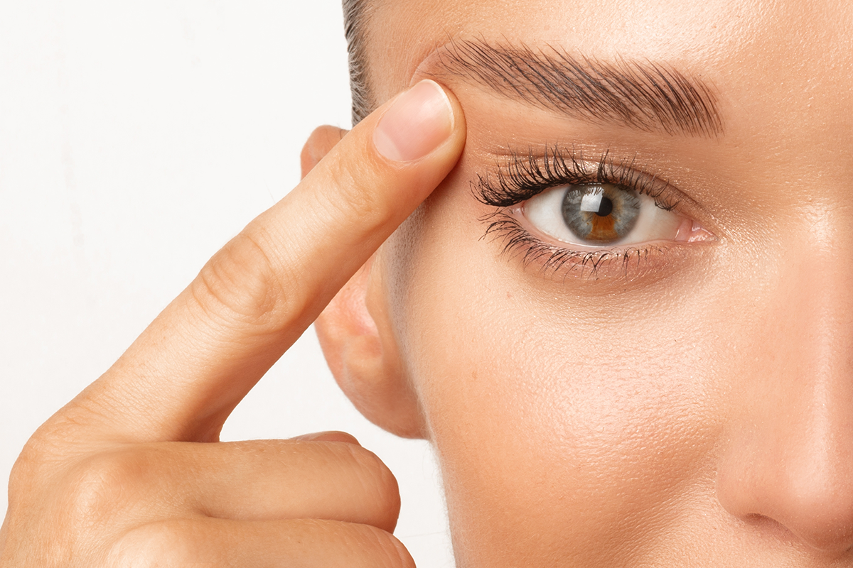 Woman with unusual eye color touching eyelid skin and pointing to the wrinkles on the upper eyelid