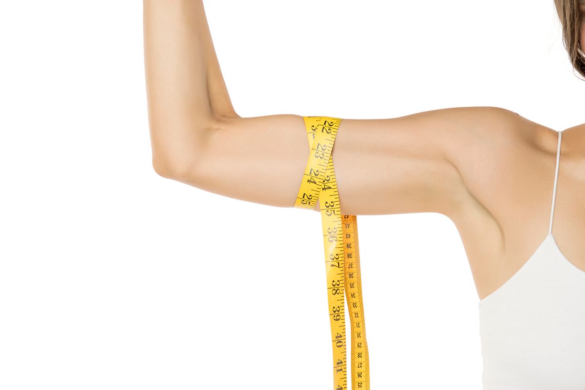 Young woman measure her biceps with a measuring tape